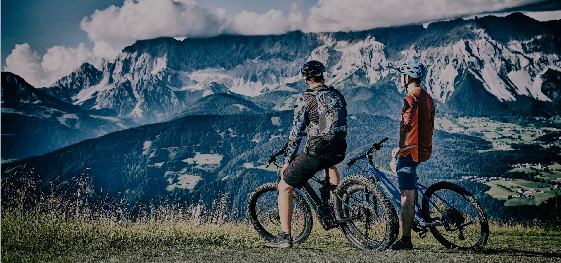 Zwei Männer sitzen auf ihren E-Bikes und schauen auf einen Berg.