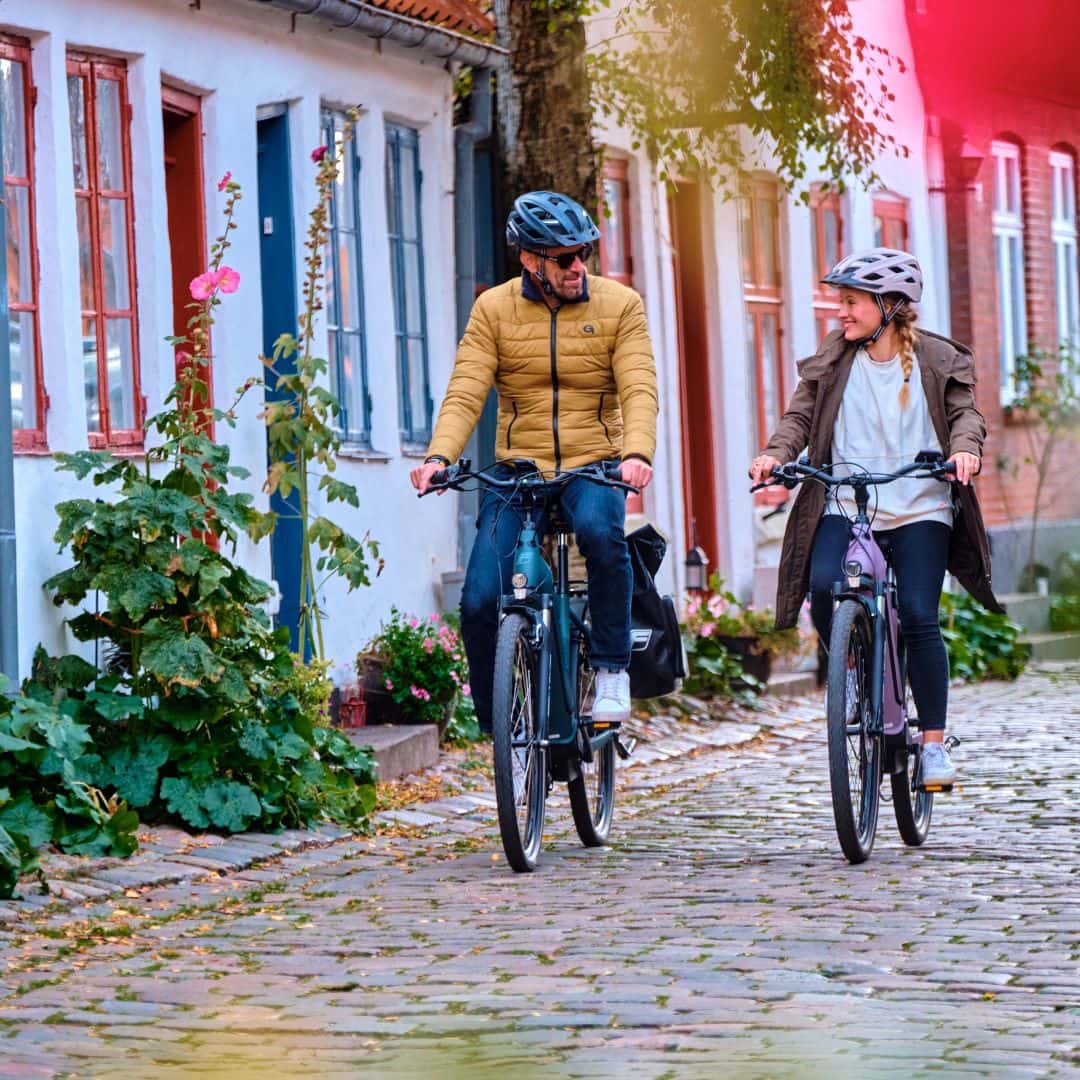 Mann und Frau fahren mit einem City E-Bike von Fischer durch die Stadt