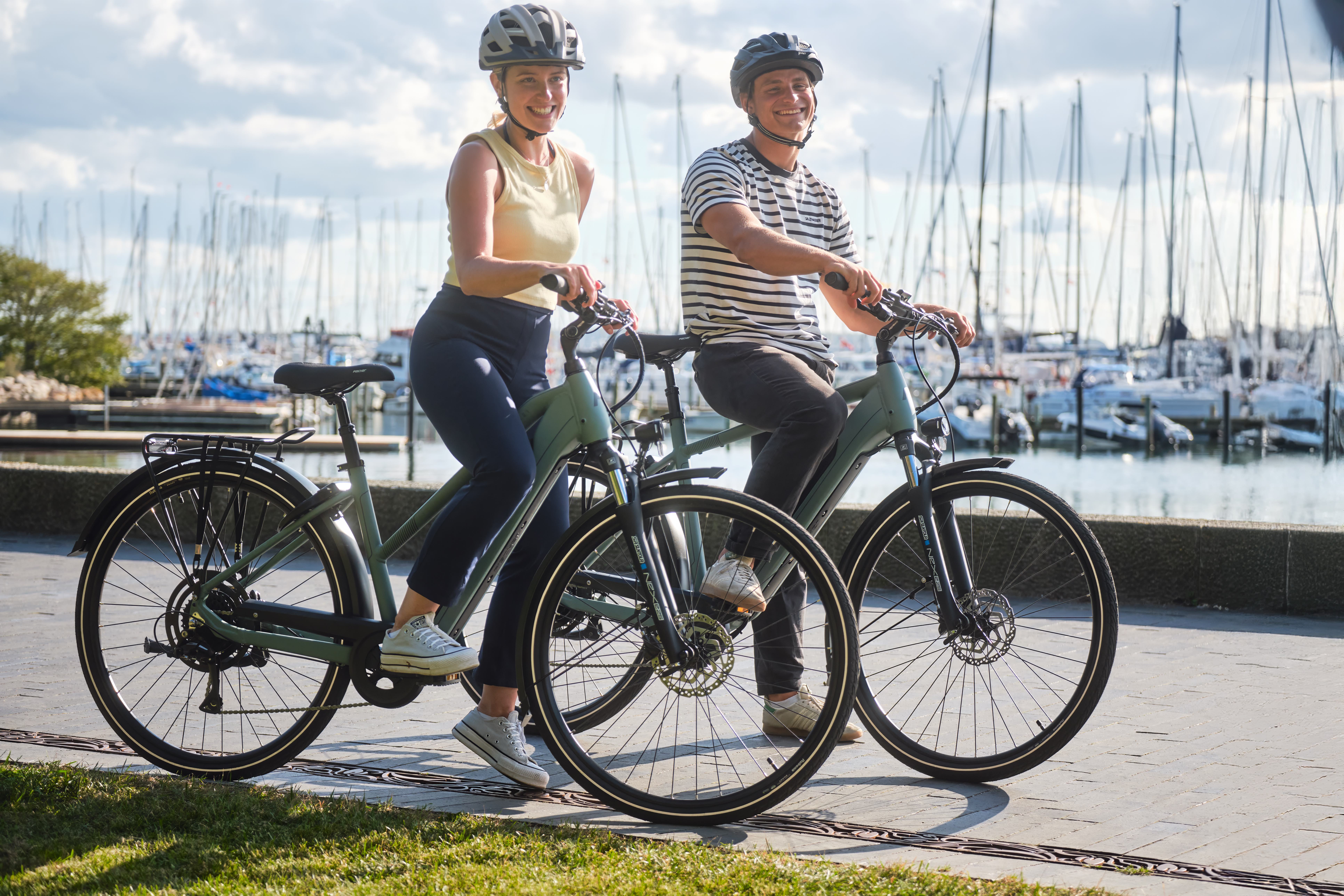 Mann und Frau stehen am Wasser mit ihren E-Bikes und lächeln