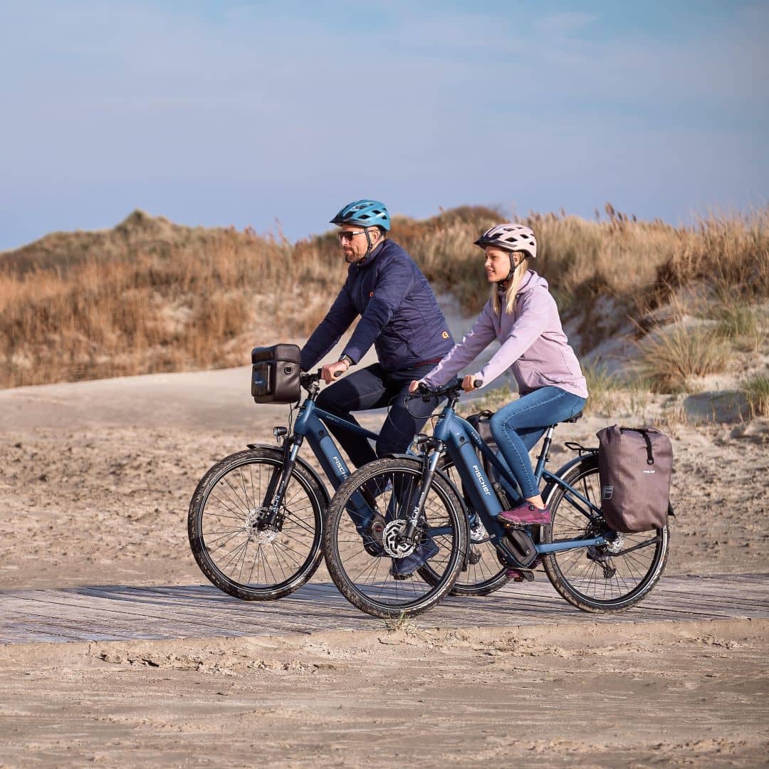 Ein Mann und eine Frau fahren mit einem Fischer E-Bike am Sandstrand entlang
